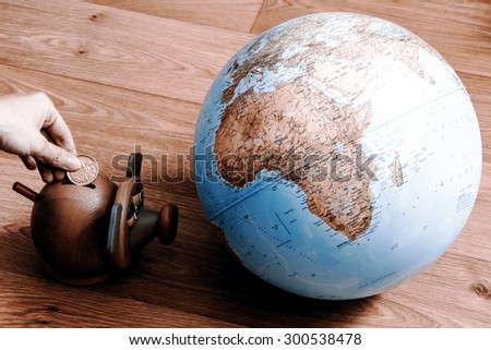 Pig money box with hand with coin and globe. Pig is staring at globe.