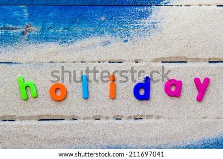 The word holiday laid sand and blue board