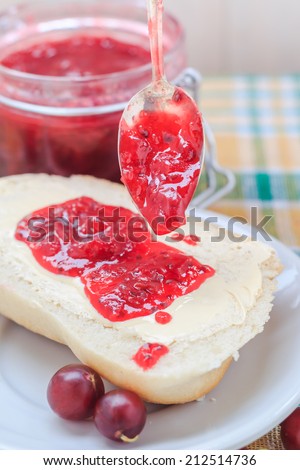 Application of gooseberry jam with a spoon on a roll