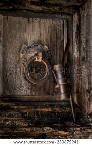Old wood door etched in Arabic with Roman letters carved below, with an original metal door knocker. The \'key holder\' is attached to the door knocker, on the door of the Church of the Holy Sepulcher.