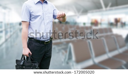 Young Businessman is waiting in the airport waiting hal and he checks the time on his watch.