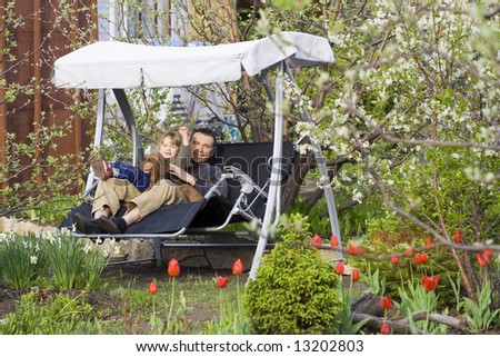 Father, his daughter and a dog have a rest in a garden relaxing swing among the spring blooming garden