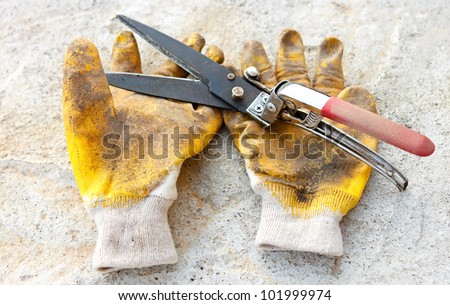 Gardening scissors and dirty yellow gloves against concrete.The working day is over.
