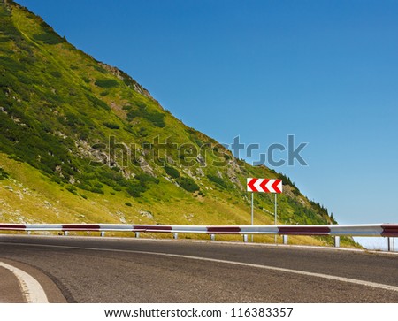 Safety sign on mountain road before a dangerous curve.Copy space for text on blue sky.