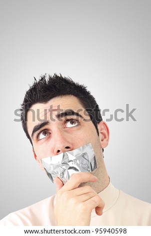 Curious young man having gray duct tape on his mouth.Gradient background with copy space.