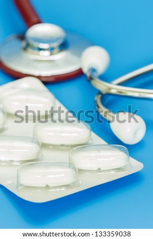 White pills in front of red stethoscope against blue background