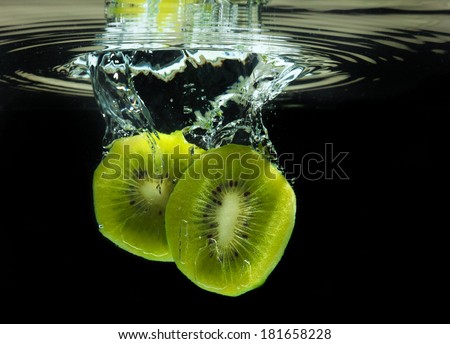 Delicious sliced kiwi dropped in fresh clean water, generating cool reflection and ripples. Black background.
