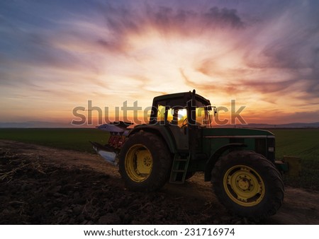 Green tractor on field at sunset after plowing