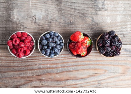 A four bowls overflowing with summer berries like strawberries, raspberries, blueberries and blackberries.