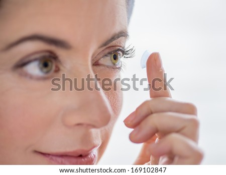 close up of an attractive mature lady putting on contact lenses in her green eyes