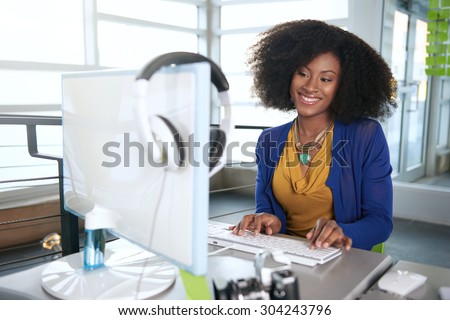 Portrait of a smiling woman with an afro at the computer in bright glass office