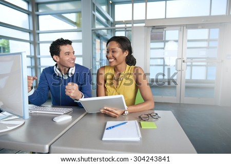 Two  colleages discussing ideas using a tablet and computer