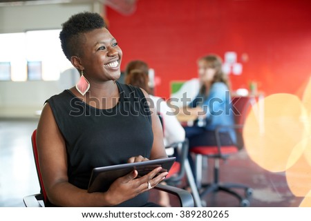 Confident female designer working on a digital tablet in red creative office space
