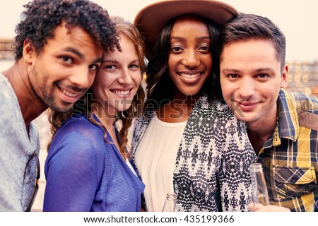 Multi-ethnic millenial group of friends taking a selfie photo with mobile phone on rooftop terrasse at sunset