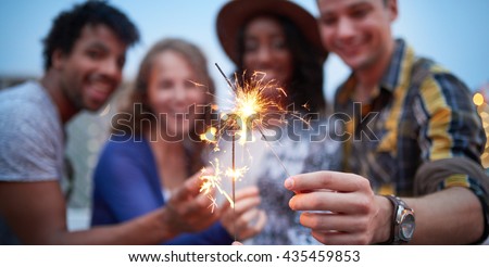Multi-ethnic millenial group of friendsfolding sparklers on rooftop terrasse at sunset