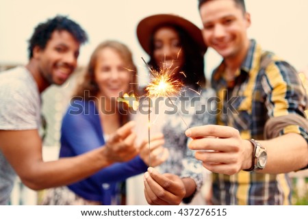 Multi-ethnic millenial group of friendsfolding sparklers on rooftop terrasse at sunset