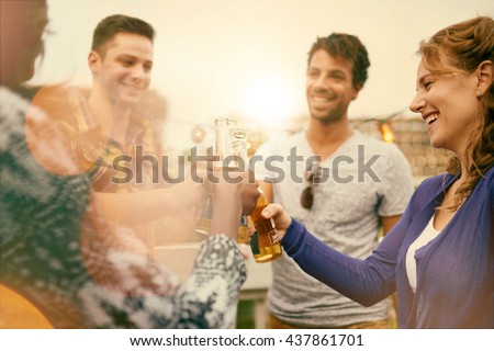 Multi-ethnic millenial group of friends partying and enjoying a beer on rooftop terrasse at sunset