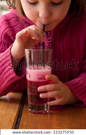 A young girl takes a delicate sip of bubbly pink lemonade through a black straw