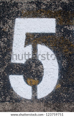 A white stencil of the number five painted on a black, grey and yellow pavement