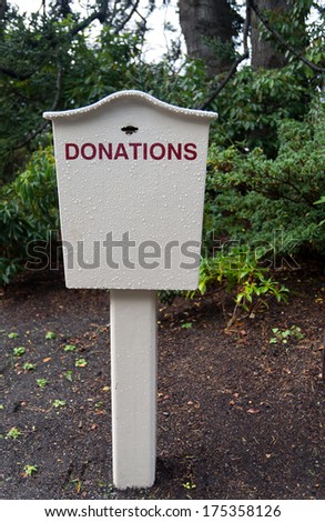 A white donations box sits in a damp garden after a shower of rain