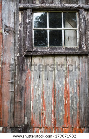 The window of an old abandoned wooden cabin with the remnants of red paint