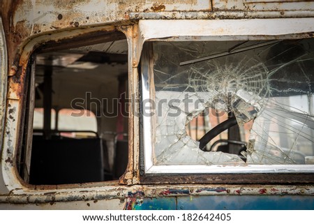 Close up detail of an old, abandoned bus showing a smashed and broken windshield.