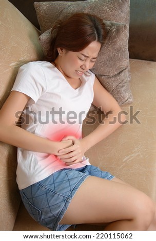Sick woman lying on sofa in the living room with stomachache with red alert accent