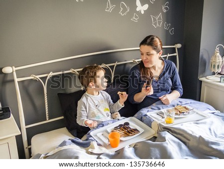 Happy mother and son having breakfast in bed at home in the morning