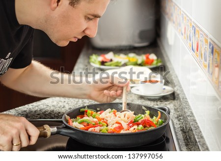 Handsome man cooking vegetables and chicken for a mexican food in a black pan