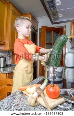 Cute child chef with apron cooking big zucchini and other vegetables in a pot on the kitchen