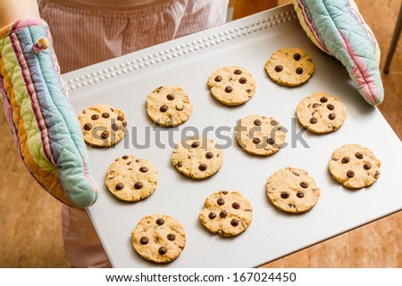Woman with colorful kitchen gloves holding a homemade baked cookies tray