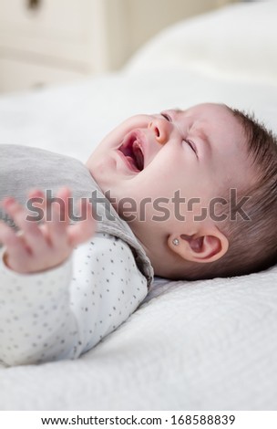 Cute baby girl crying over white bedcover
