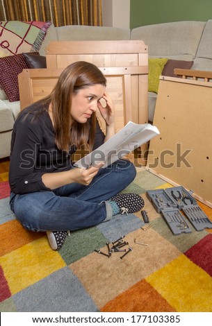Surprised girl with tools reading the instructions to assemble a new furniture for home