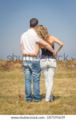 Back view of beautiful love couple embracing and looking the sky outdoors on a summer day