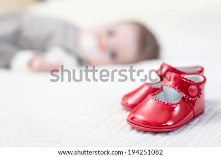 Closeup of baby red patent leather shoes over a bed and adorable babe lying on the background