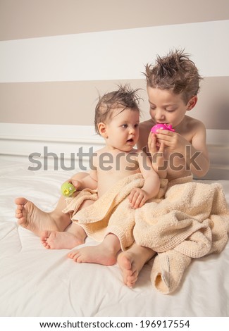 Portrait of sweet boy and little girl with wet hair under the towels playing over a bed after bath