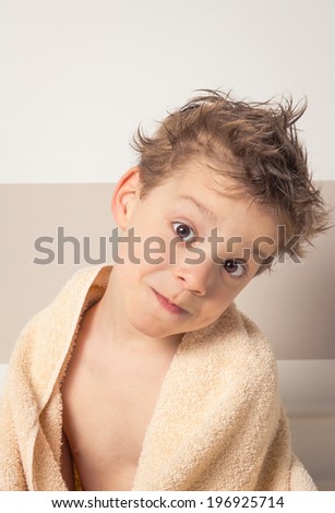 Portrait of sweet boy with wet hair under the towel over a bed after bath