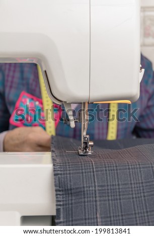 Closeup of sewing machine needle and seamstress hands working with clothing item on the backgroud