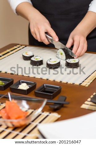 Closeup of woman chef cutting japanese sushi rolls with rice, avocado and shrimps on nori seaweed sheet
