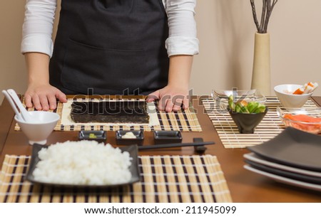 Woman chef ready to prepare japanese sushi rolls, with principal ingredients in the foreground. Selective focus in nori seaweed