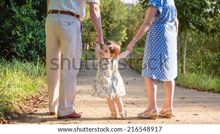 Portrait of baby granddaughter walking with her grandparents on a nature path