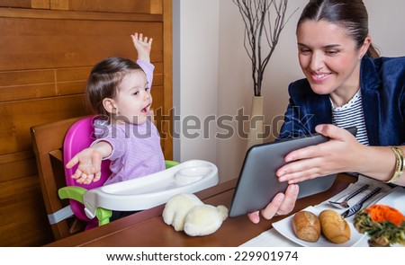 Businesswoman mother and happy baby girl looking tablet computer sitting in a restaurant table