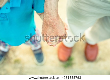 Child holding hand of senior man over a nature path background. Two different generations concept.