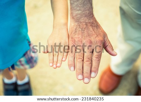 Child and senior man comparing his hands size over a nature path background. Two different generations concept.