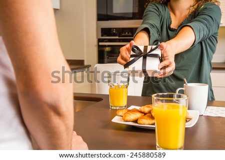 Closeup of woman hands giving a gift box to her boyfriend while having breakfast in the home kitchen