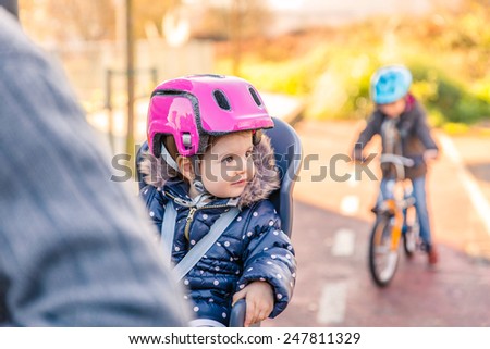 Portrait of little girl with security helmet on the head sitting in bike seat and her brother with bicycle on the background. Safe and child protection concept