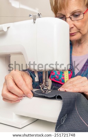 Senior seamstress woman working with clothing item on a sewing machine
