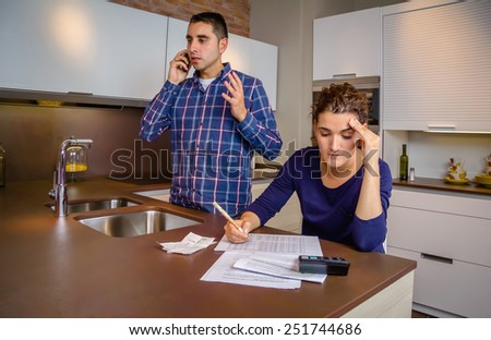 Angry young man arguing at phone while a woman calculating their bank credit lines. Financial family problems concept.
