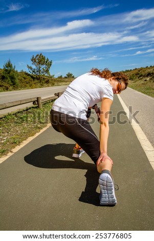 Back view of athletic young woman with sportswear suffering pain in her leg calf by a muscle cramp on a training. Sport injuries concept.
