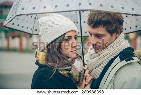 Portrait of young beautiful couple in love looking under the umbrella in an autumn rainy day. Love and couple relationships concept.